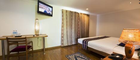 Una habitación de hotel con cama, escritorio, silla, lámpara y televisor.