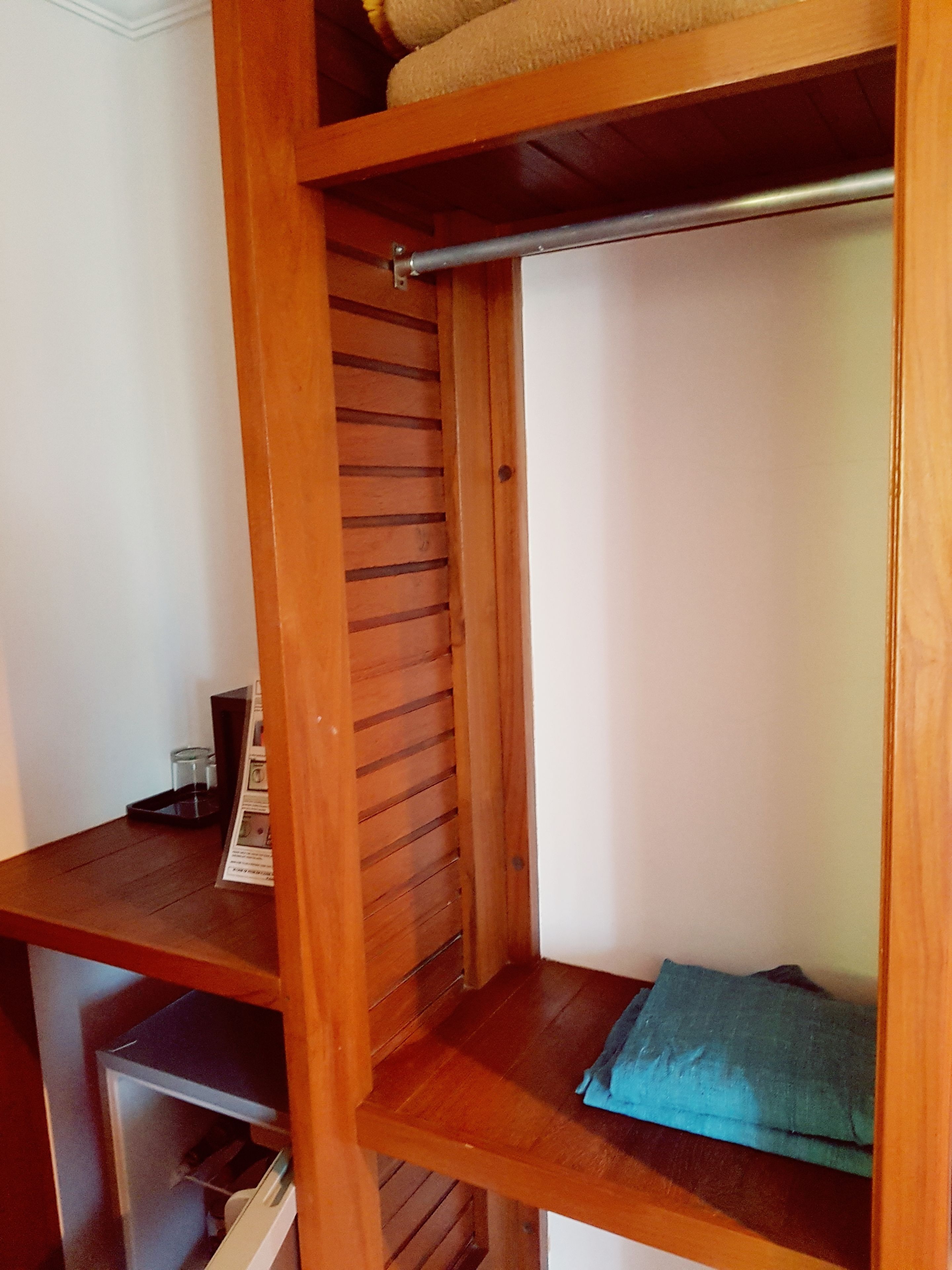 A wooden closet with a hanging rod and shelves.