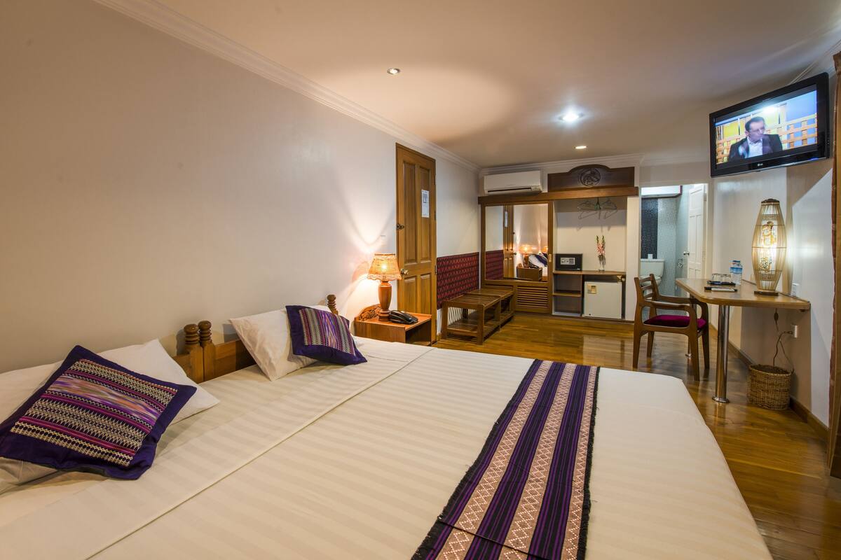 A hotel room with a large bed, a desk with a computer, a television, and a small kitchenette.
