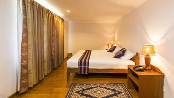 Una habitación de hotel con cama, mesita de noche, lámpara y una alfombra estampada.