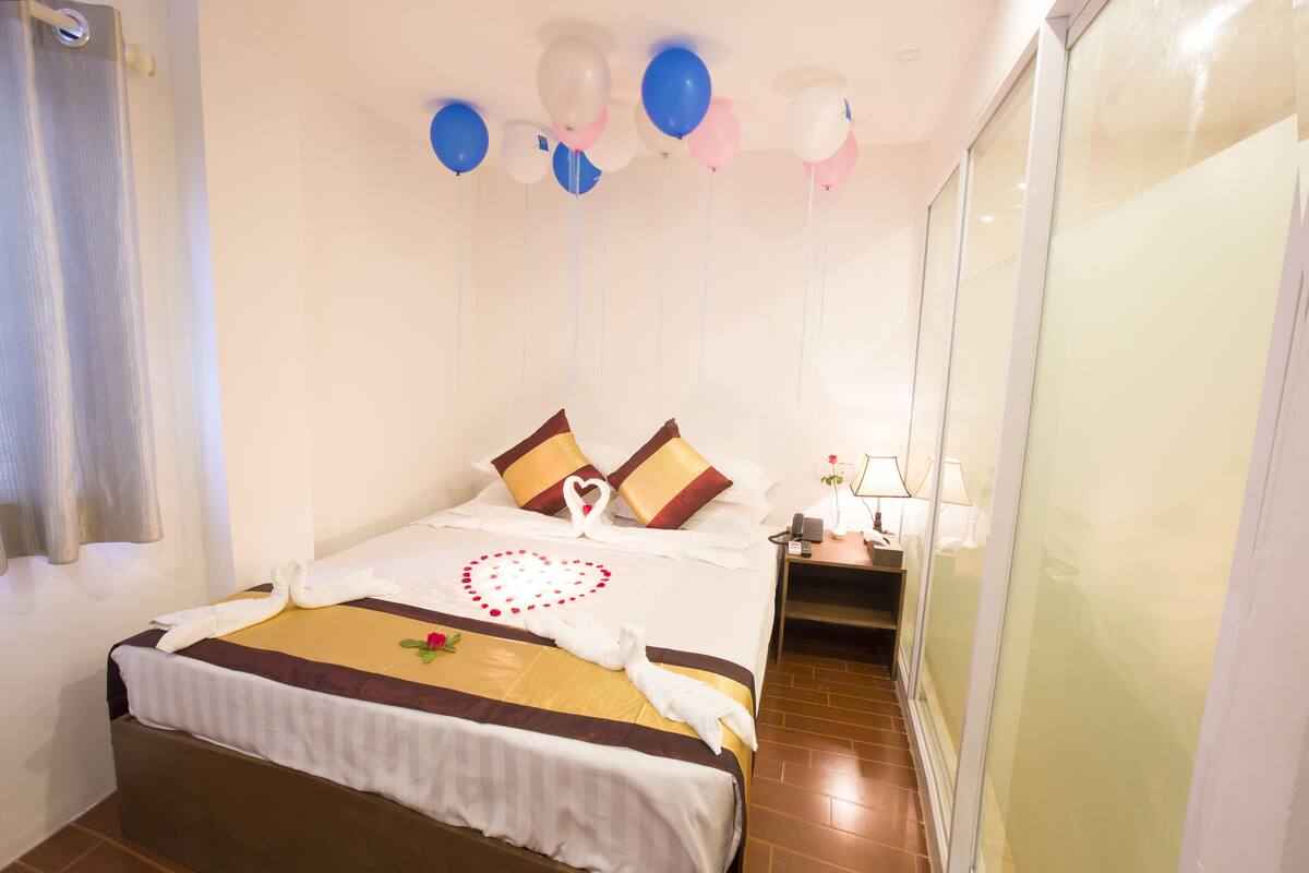 Une chambre d’hôtel avec un lit, une table de chevet, une lampe et une cloison en verre.