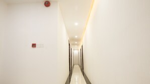 A long, narrow hallway with white walls and a shiny floor. There are light fixtures on the ceiling and a fire alarm on the wall. - Hotel Sunny Mandalay (Mandalay)