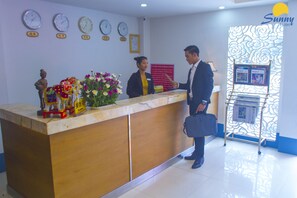 Un mostrador de recepción de hotel con relojes, una composición floral y una estatua decorativa.