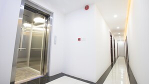 A clean, modern hallway with a shiny floor, a glass elevator, and a fire alarm on the wall. - Hotel Sunny Mandalay (Mandalay)