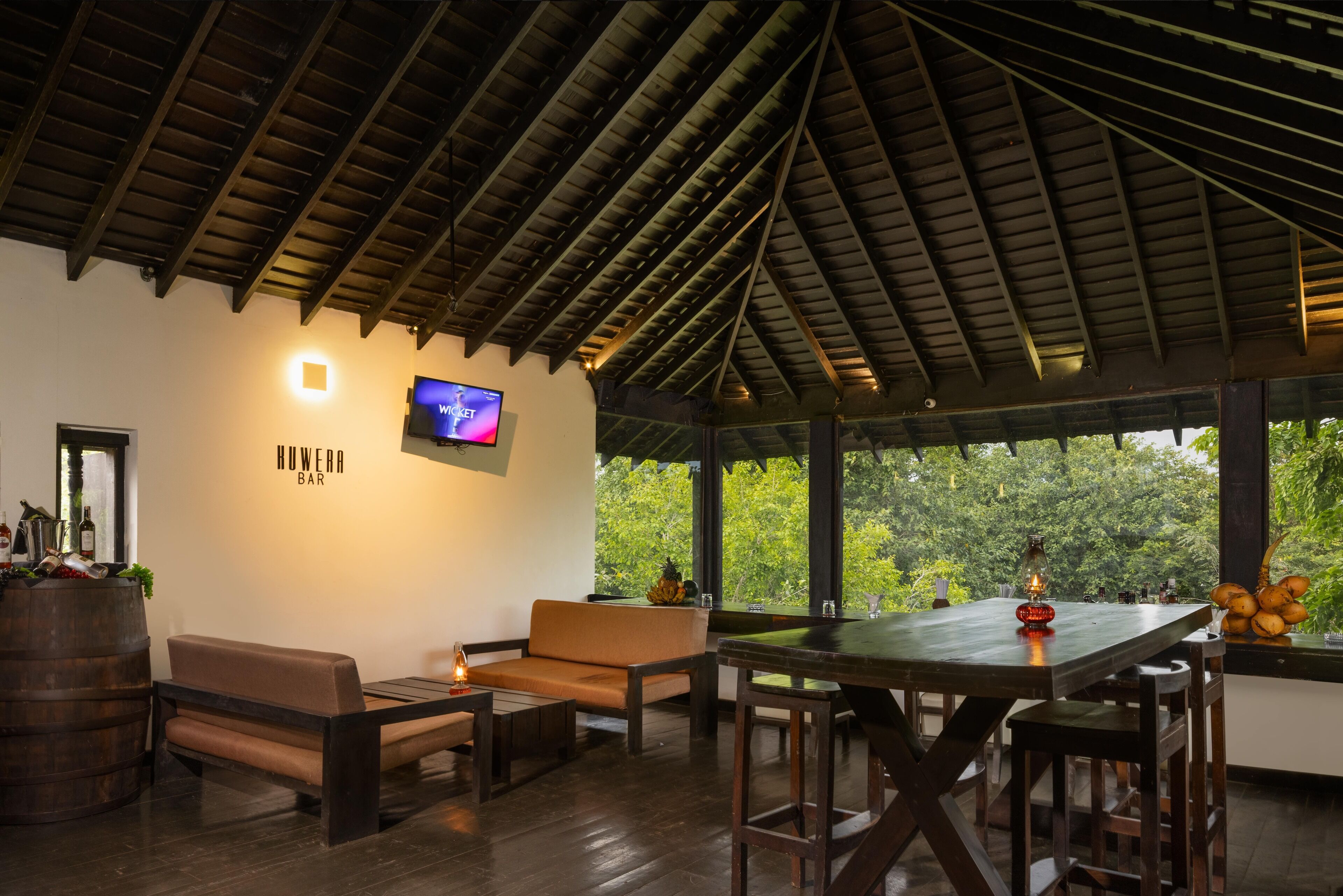 A bar area with wooden furniture, a television, and a view of greenery outside.