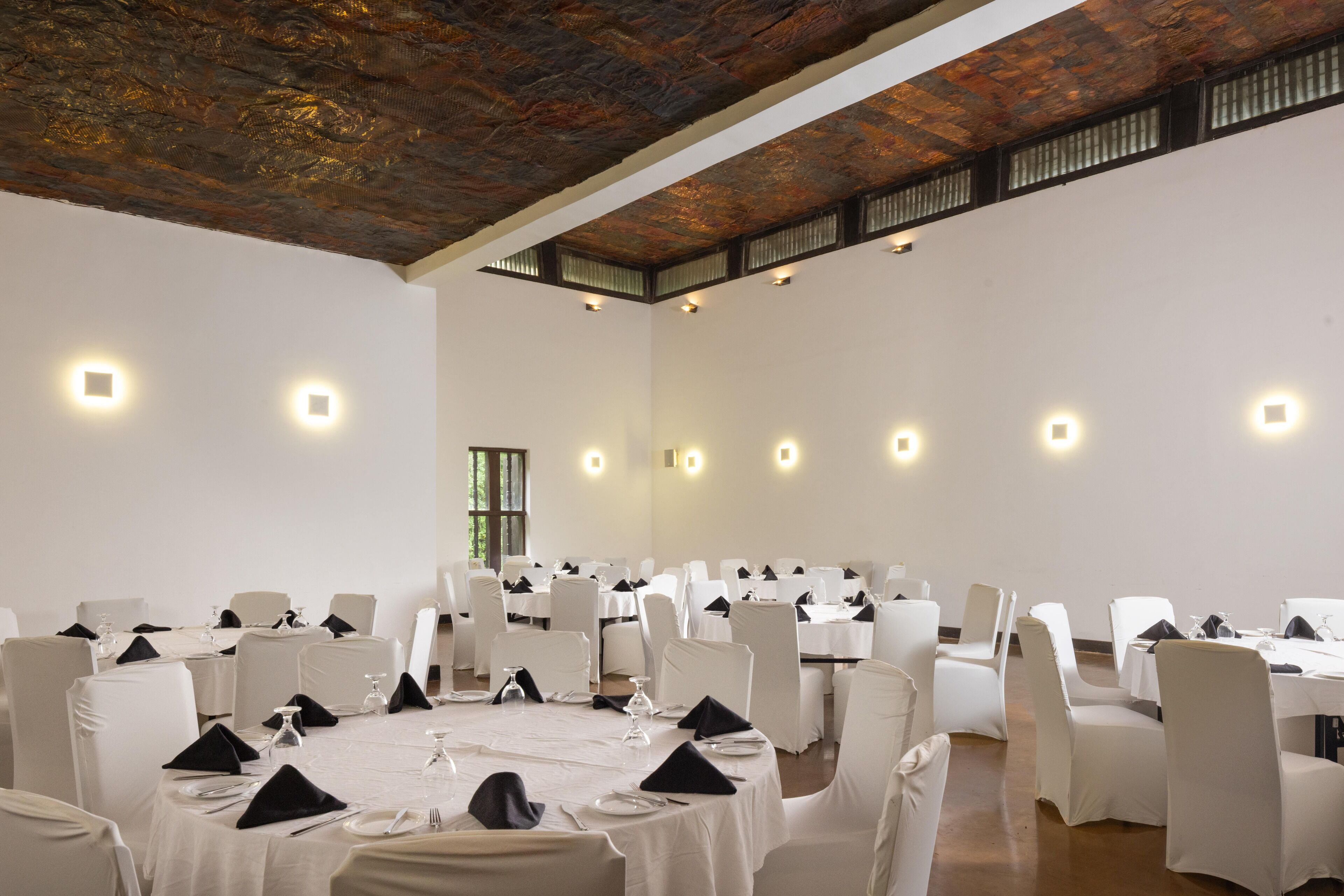 Un gran salón de banquetes con mesas redondas, sillas blancas y pequeñas luces en las paredes.