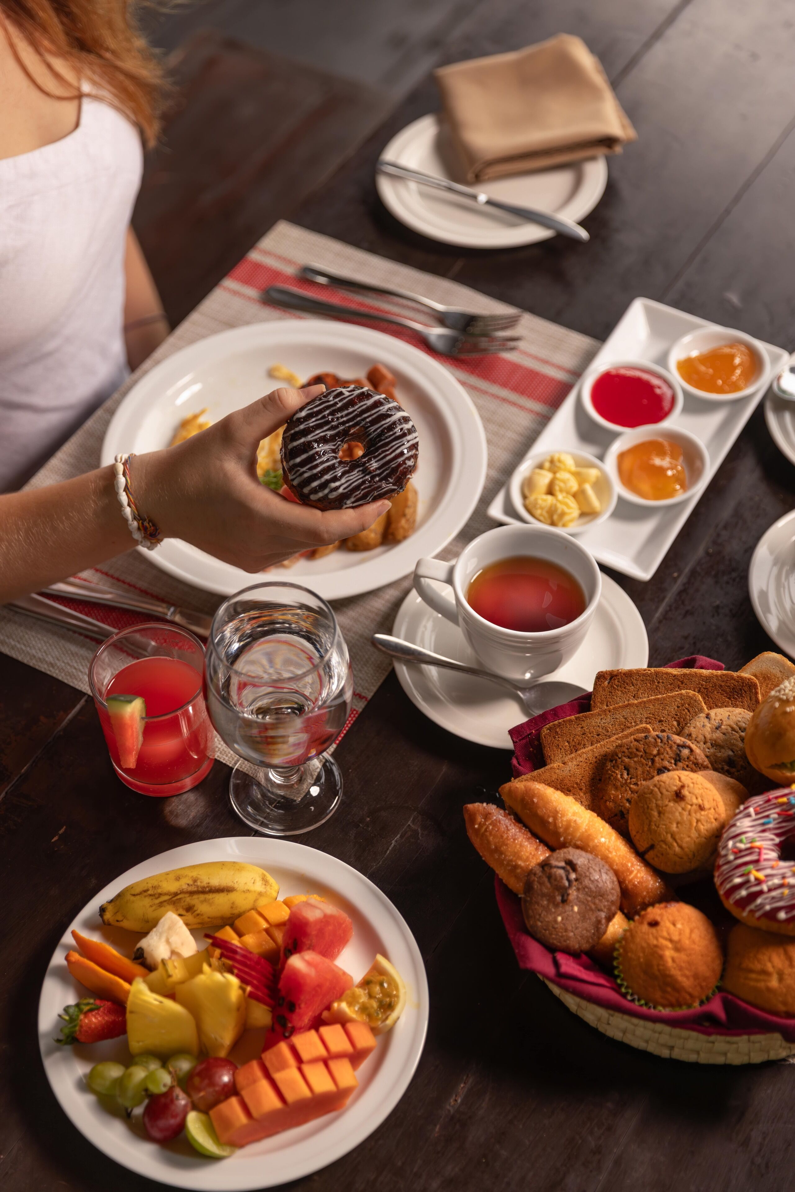 A table set with breakfast items including a plate of fruit, muffins, and a donut.