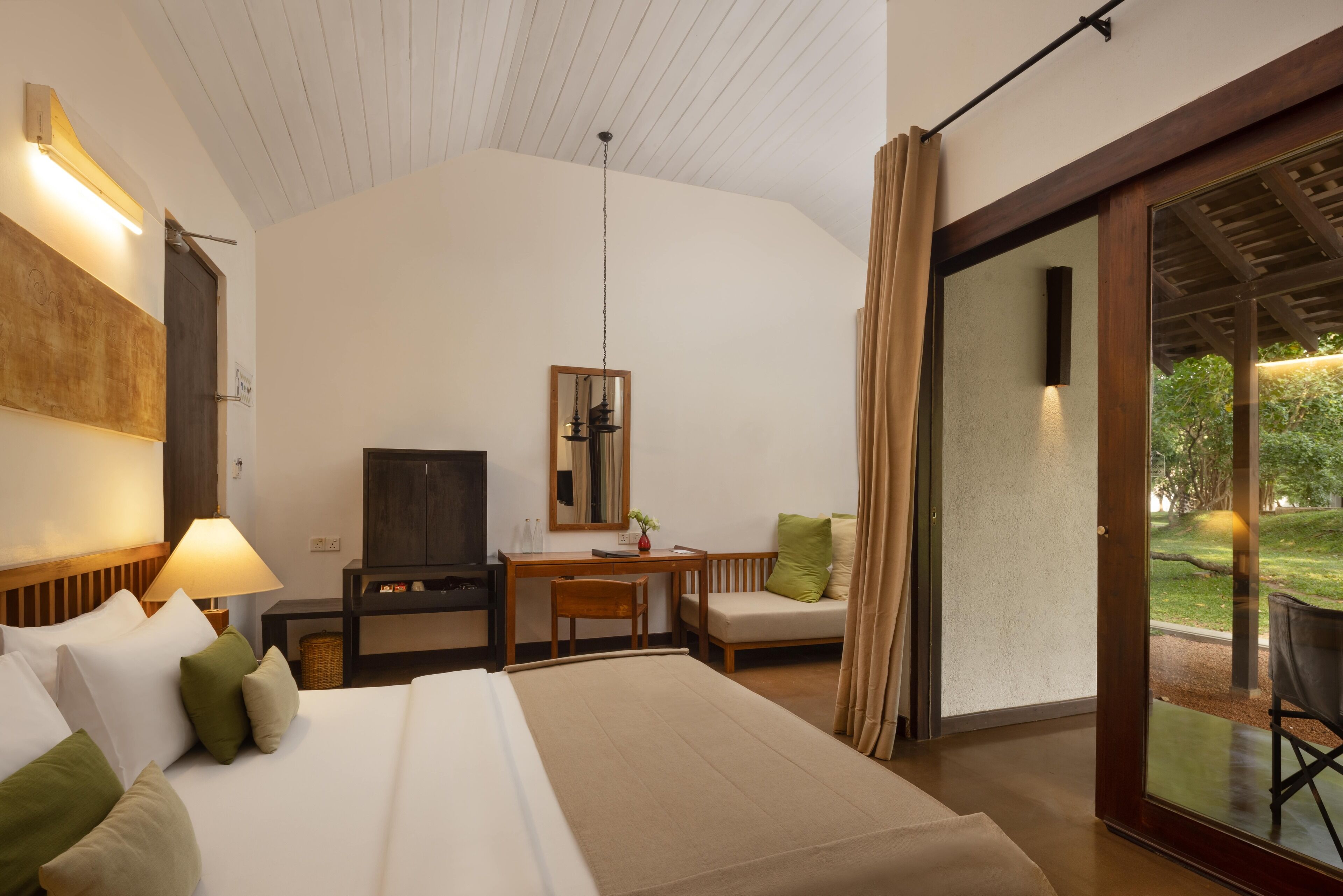 Habitación de hotel con cama, escritorio, silla y puerta corrediza de vidrio que da a un espacio al aire libre.