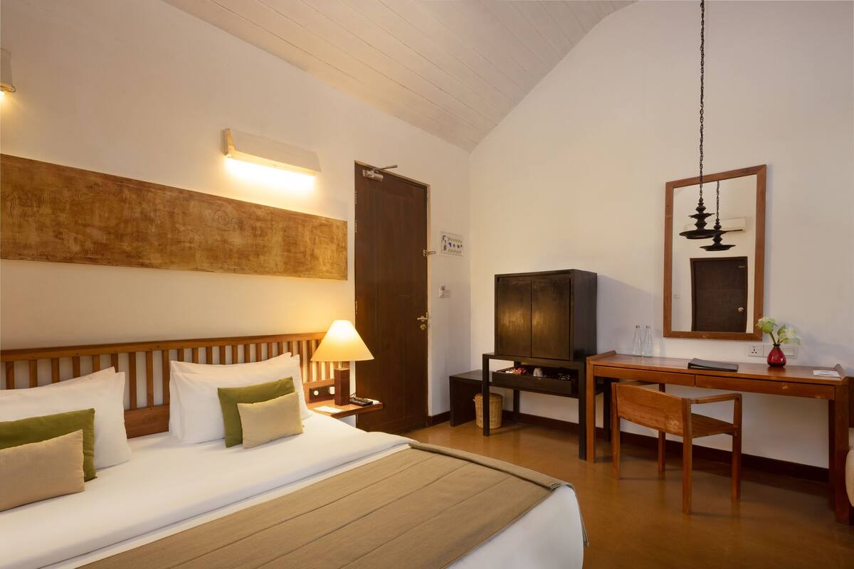 A hotel room with a bed, bedside table, lamp, television, desk, chair, and a mirror on the wall.