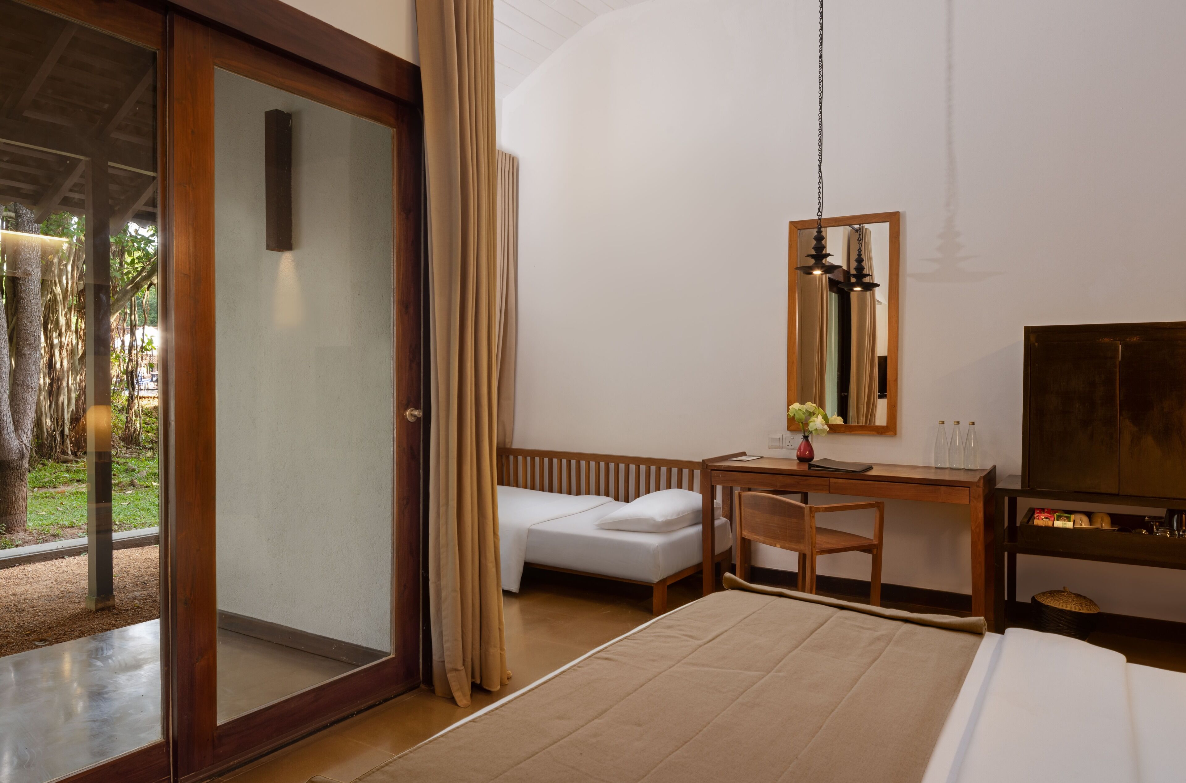 A hotel room with a bed, a desk, a chair, a TV, and a sliding glass door leading to an outdoor area.