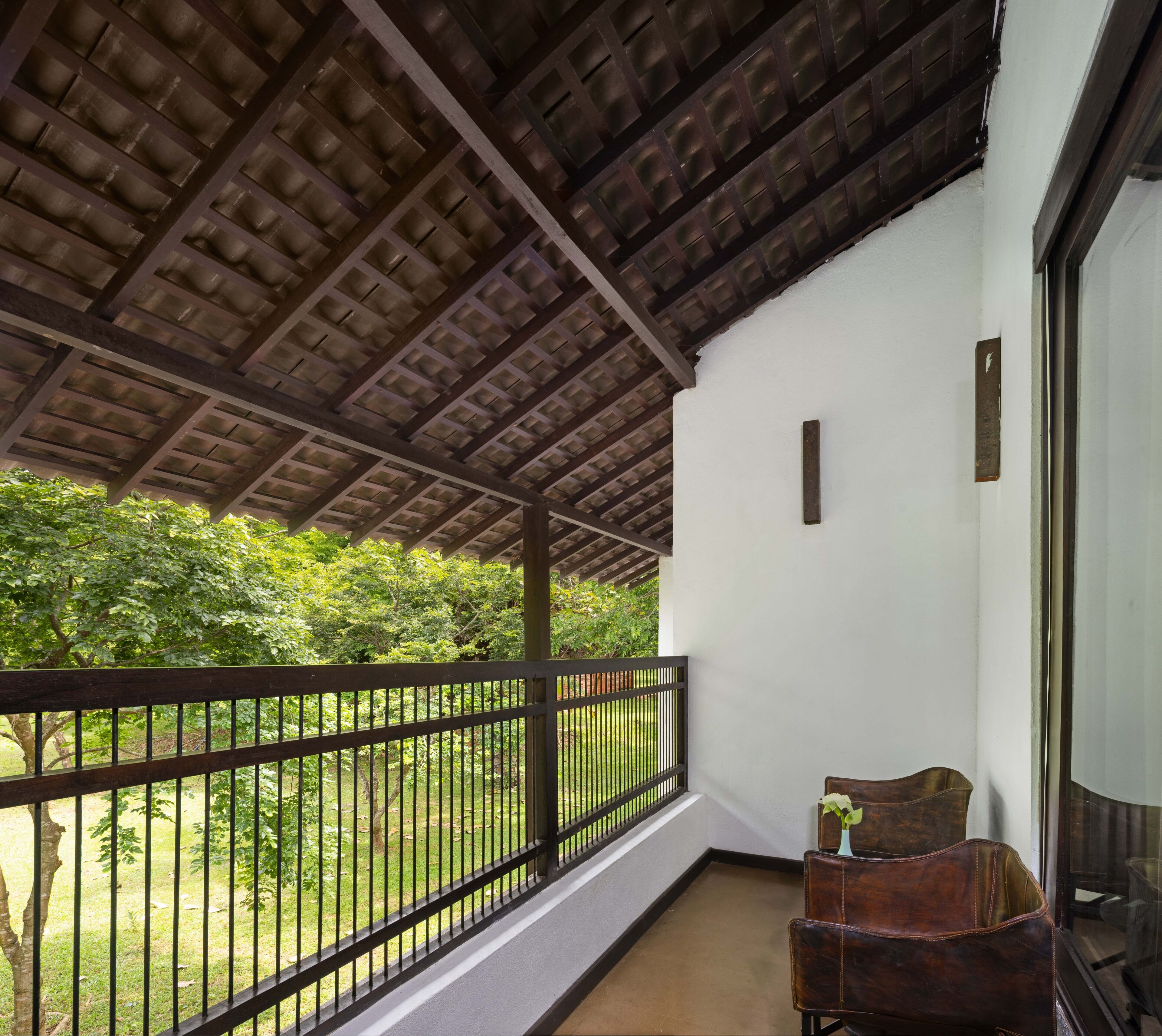 A balcony with a wooden ceiling, a metal railing, and a view of a green landscape.