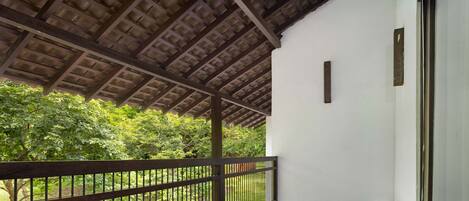 A balcony with a wooden ceiling, a metal railing, and a view of a green landscape.