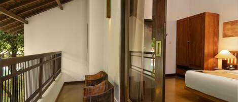 A balcony with a wooden railing, a wooden chair, and a glass door leading to a bedroom with a bed and a wooden wardrobe.