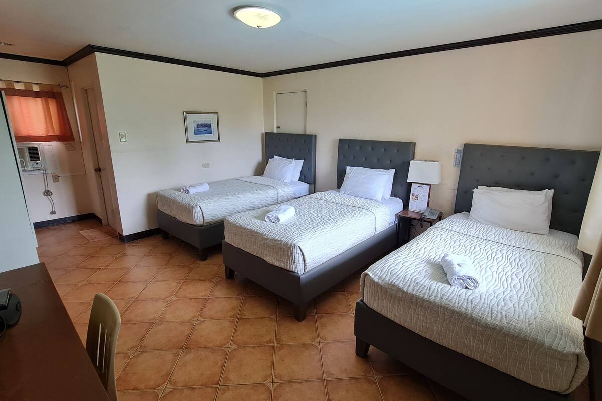 Habitación de hotel con dos camas, un escritorio, una silla y un baño visible a través de una puerta abierta.