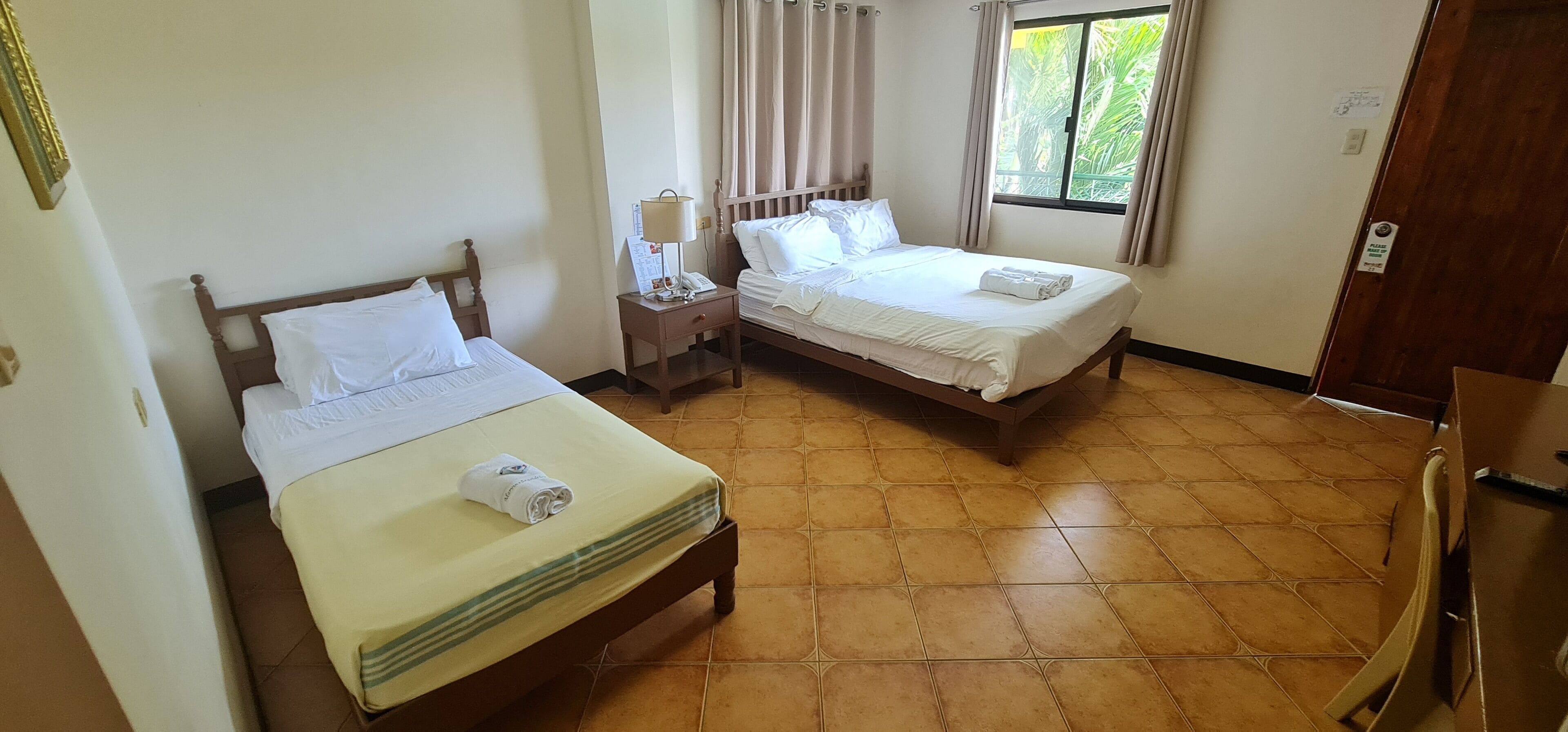 A hotel room with two beds, a nightstand with a lamp, and a window with curtains.