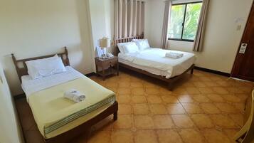 A hotel room with two beds, a nightstand with a lamp, and a window with curtains.