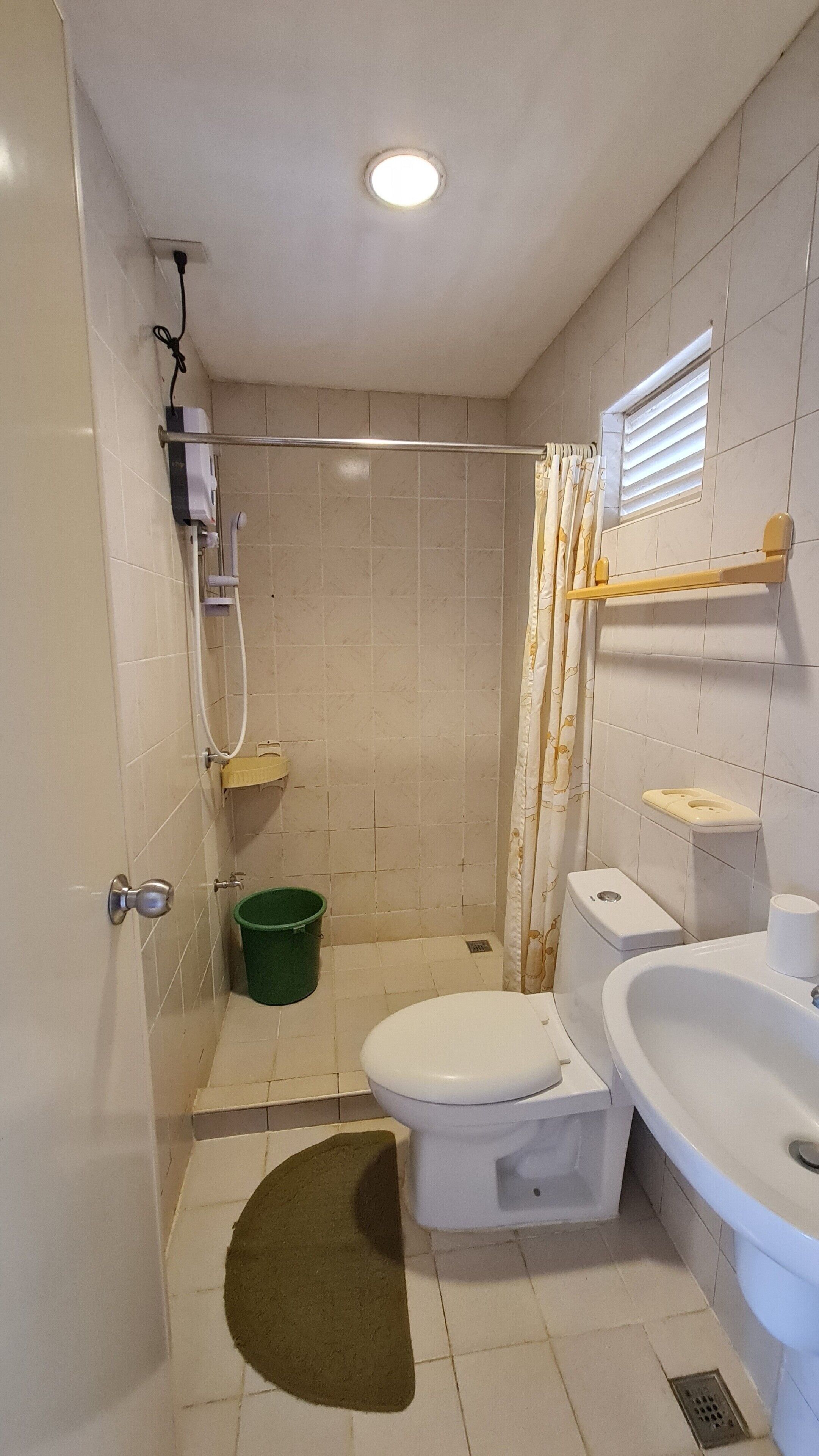 Un baño pequeño con inodoro, lavabo, ducha y un cubo verde.