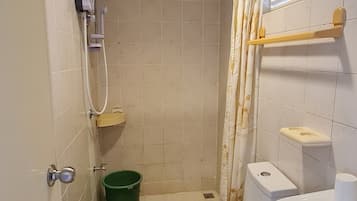Un baño pequeño con inodoro, lavabo, ducha y un cubo verde.
