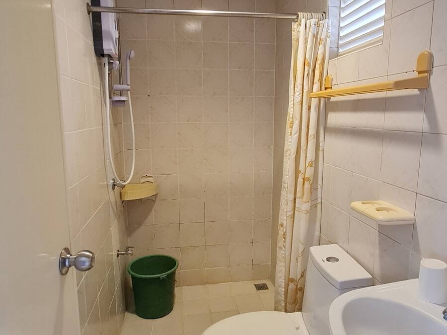Un baño pequeño con inodoro, lavabo, ducha y un cubo verde.