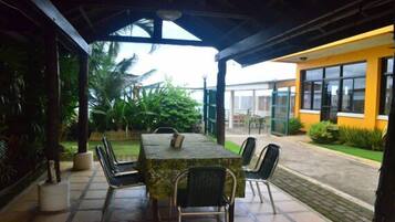 An outdoor patio with a table and chairs, surrounded by greenery and a building in the background.
