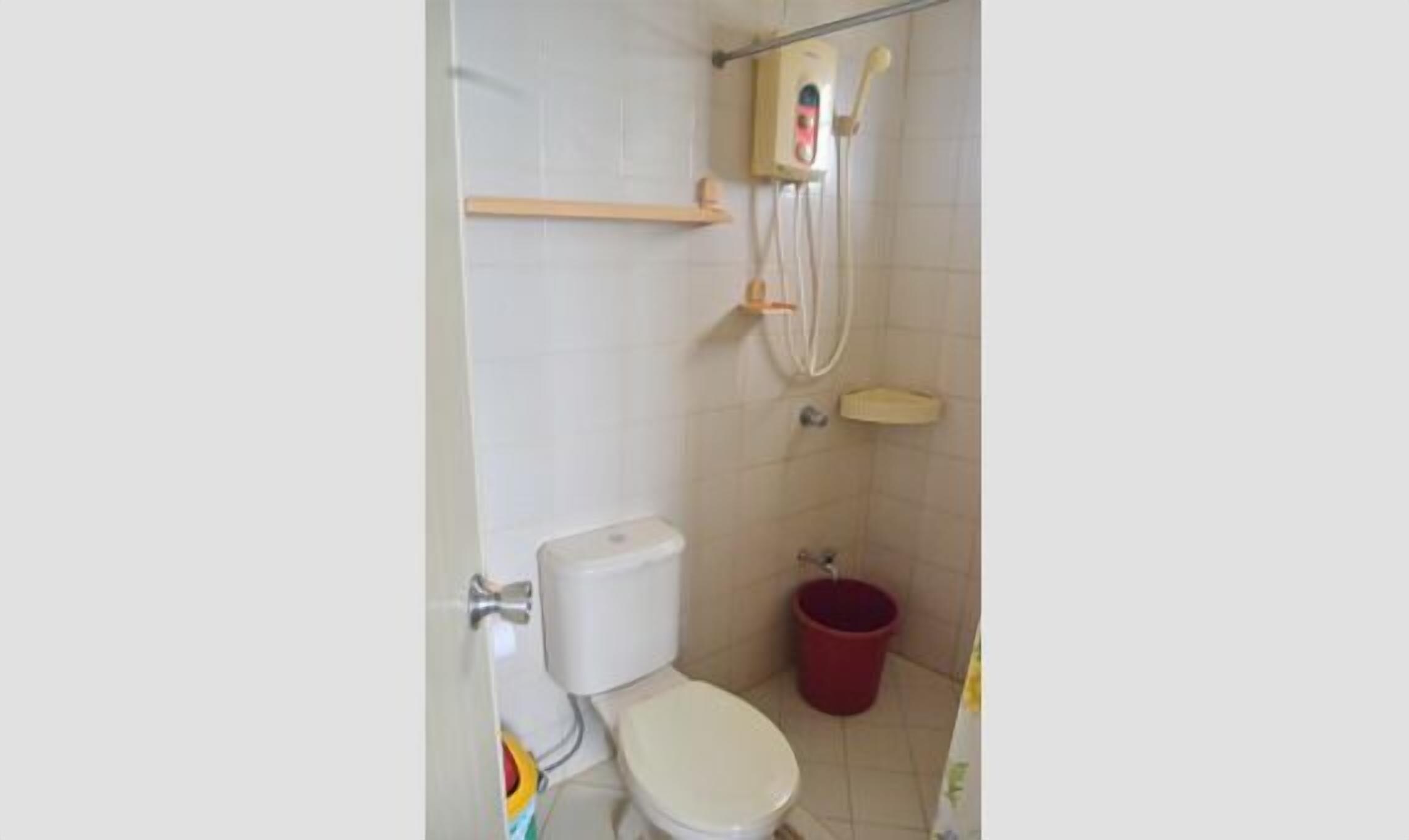A small bathroom with a toilet, a shower, and a red bucket.