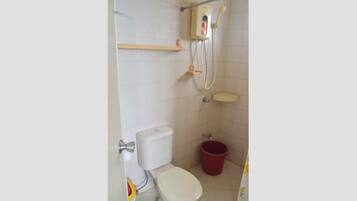 A small bathroom with a toilet, a shower, and a red bucket.
