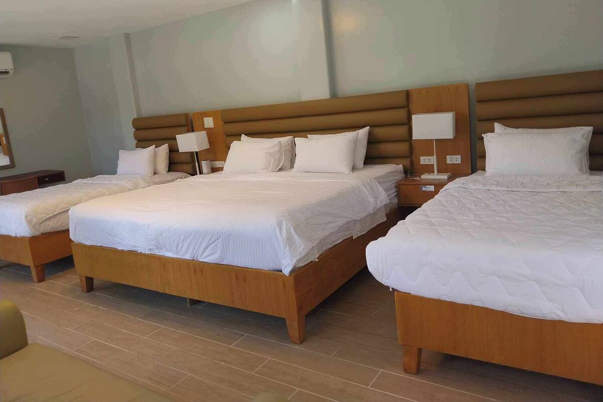 Habitación de hotel con tres camas de madera, cada una con ropa de cama blanca y mesitas de noche con lámparas.