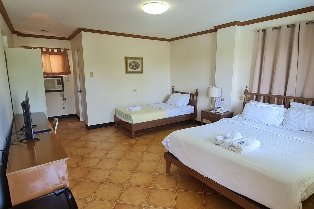 Habitación de hotel con dos camas individuales, un escritorio con una computadora, una silla y una mesita.