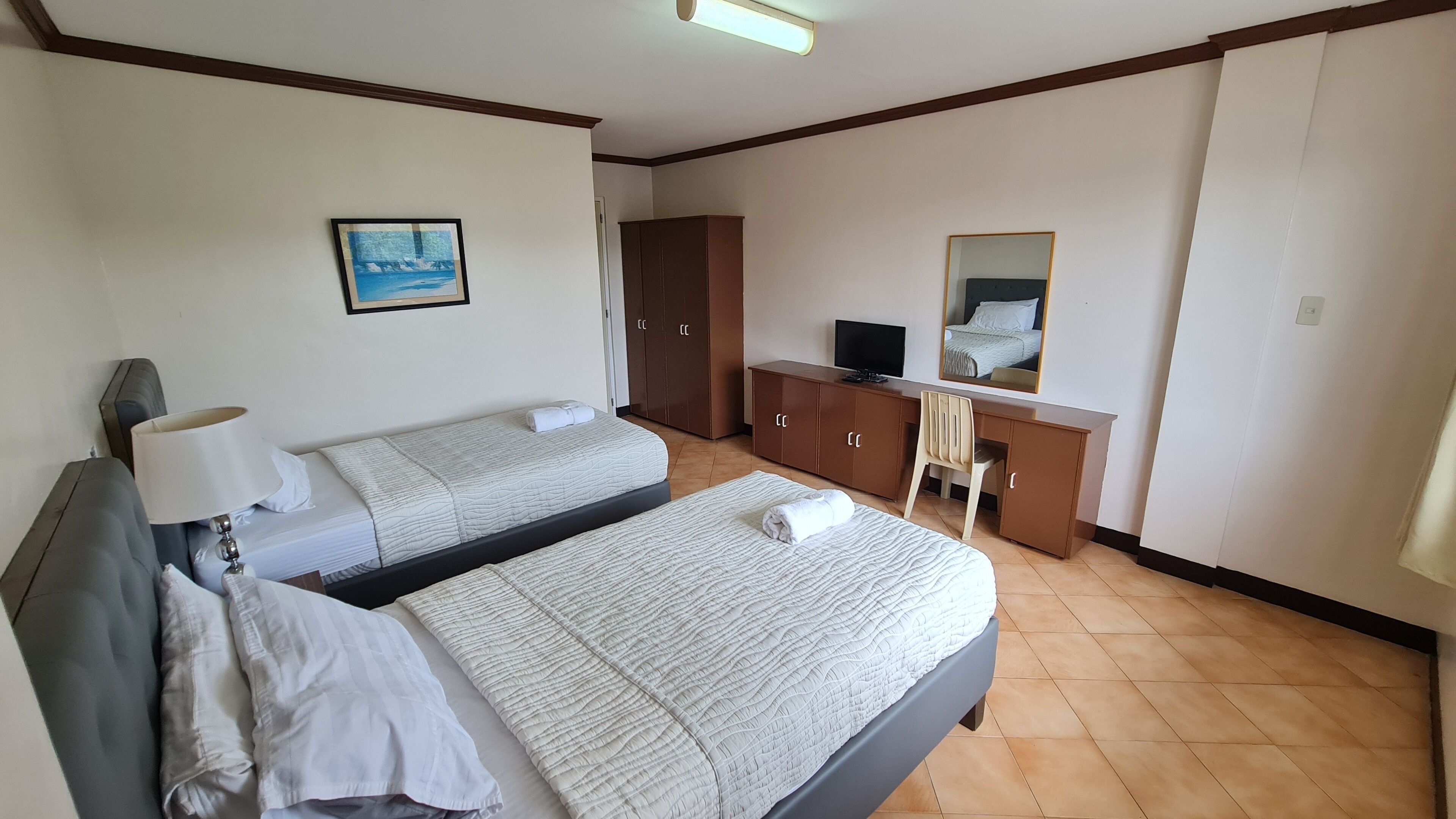 Een hotelkamer met twee bedden, een bureau, een stoel, een televisie en een kledingkast.