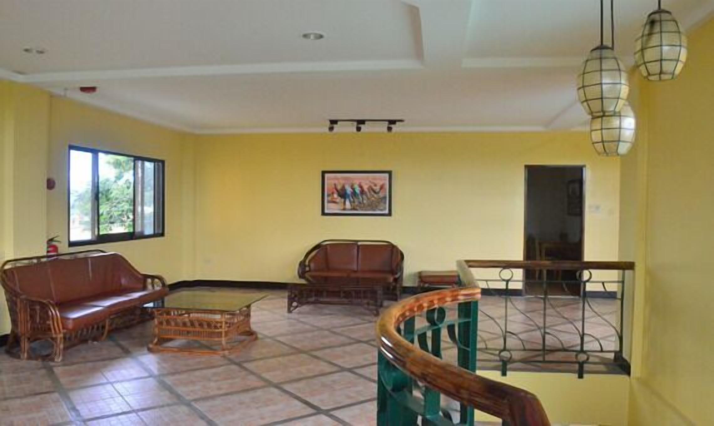 A spacious living area with a high ceiling, a large window, a wooden sofa, a wicker chair, and a staircase with a metal railing.