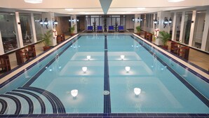 Una piscina interior con carriles delimitados, sillones de descanso y plantas en macetas.