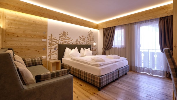 A cozy bedroom with a bed, a sofa, and a wooden floor. - Cimon Dolomites Hotel (Predazzo)