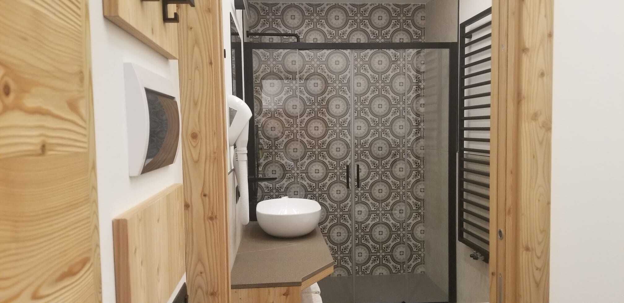 A modern bathroom with a wooden vanity, a white sink, and patterned tiles.