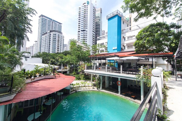 Un área de piscina en la azotea, con techo rojo, rodeada de vegetación y vistas a un paisaje urbano con edificios altos.