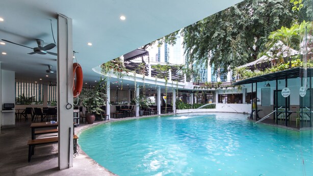 Una piscina interior con ventilador de techo, un flotador salvavidas y vistas a un edificio con vegetación.