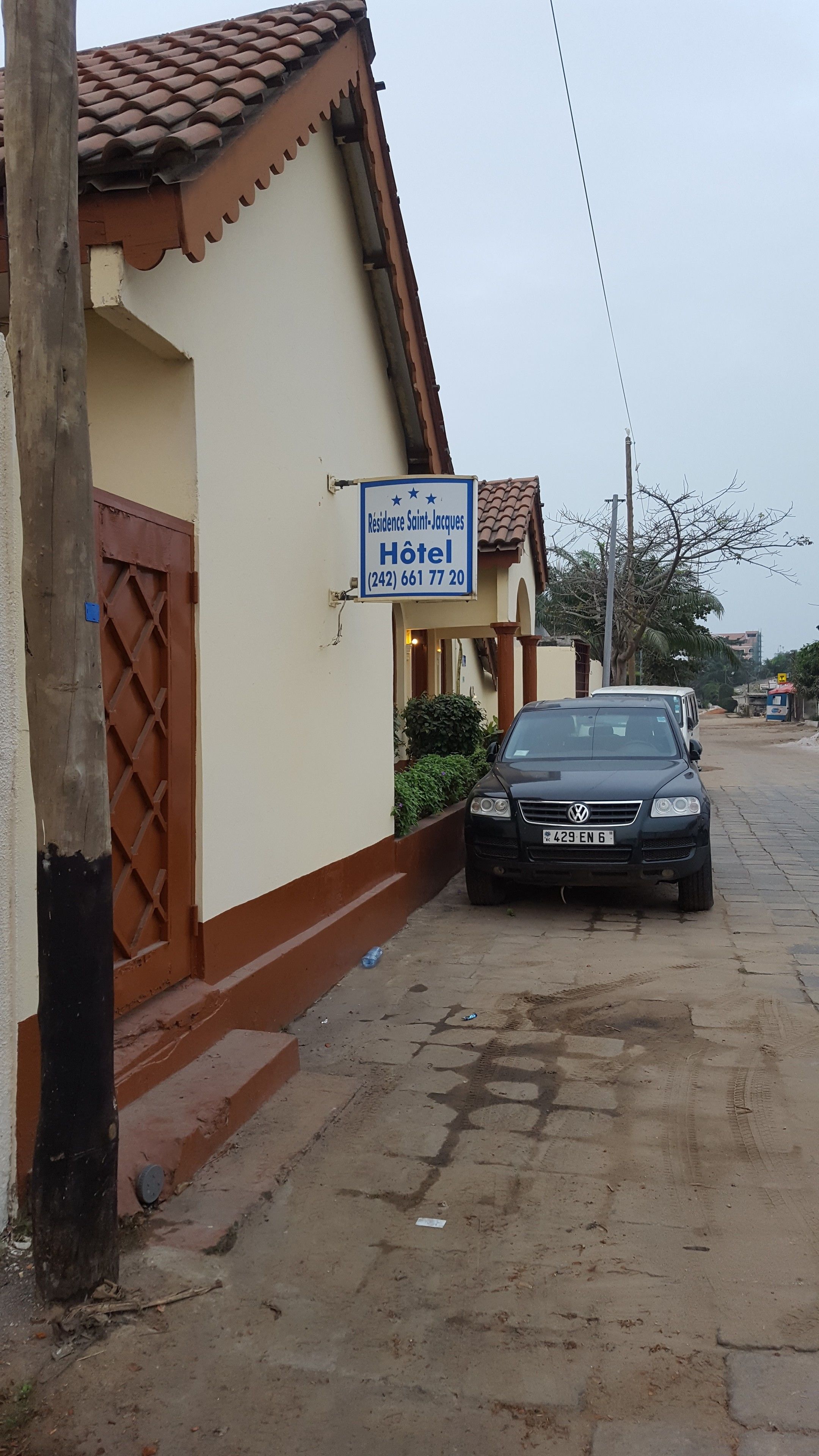 A hotel sign, a black car parked in front, and a building with a tiled roof.