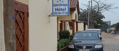 A hotel sign, a black car parked in front, and a building with a tiled roof.