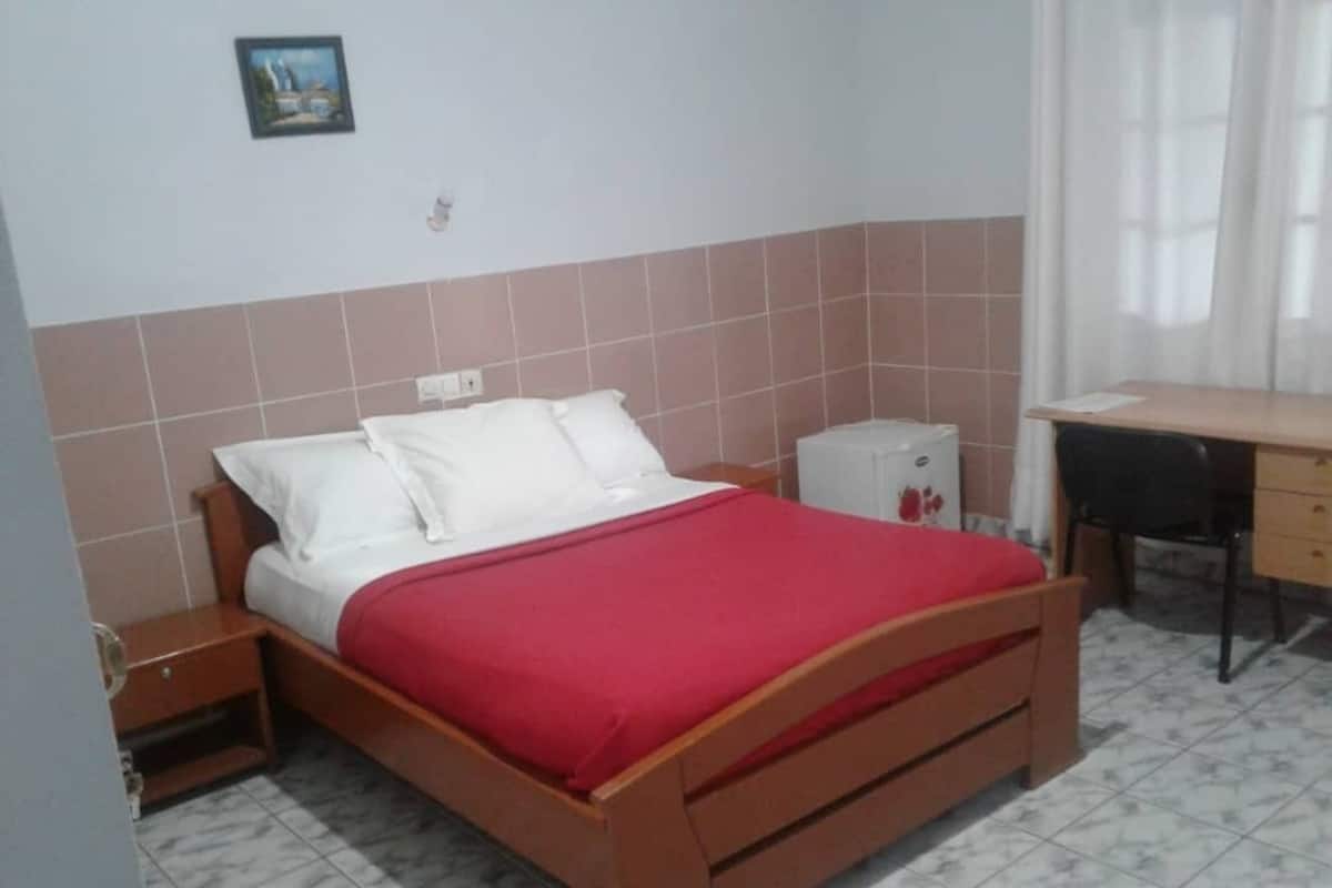 A bedroom with a wooden bed, a nightstand, a desk, and a small cabinet.