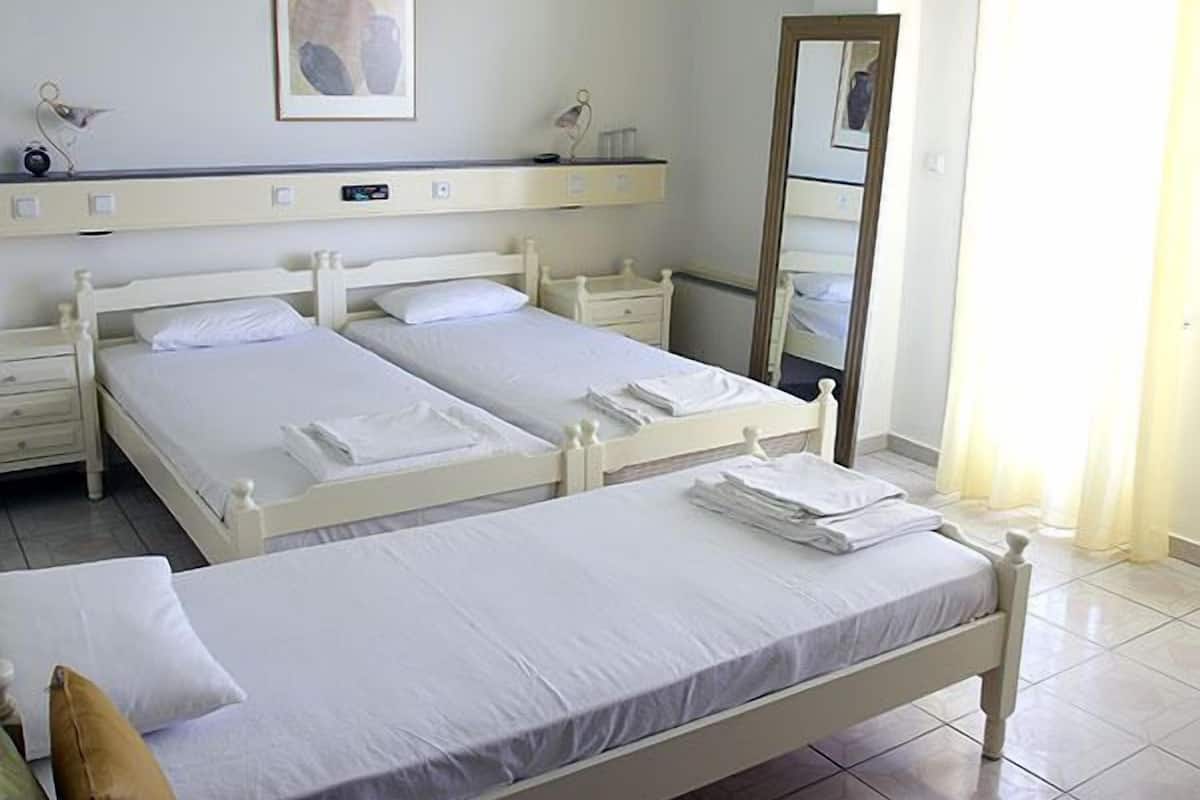 A hotel room with two single beds, a bedside table with a lamp, a mirror, and a framed picture on the wall.