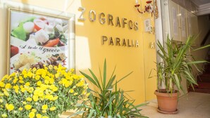 A yellow wall with the name 'Zografos Paralia' and a framed picture of food. There is a potted plant in the foreground. - Hotel Zografos (Katerini)