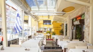 A restaurant with outdoor seating, a yellow interior, and a view of the street. - Hotel Zografos (Katerini)