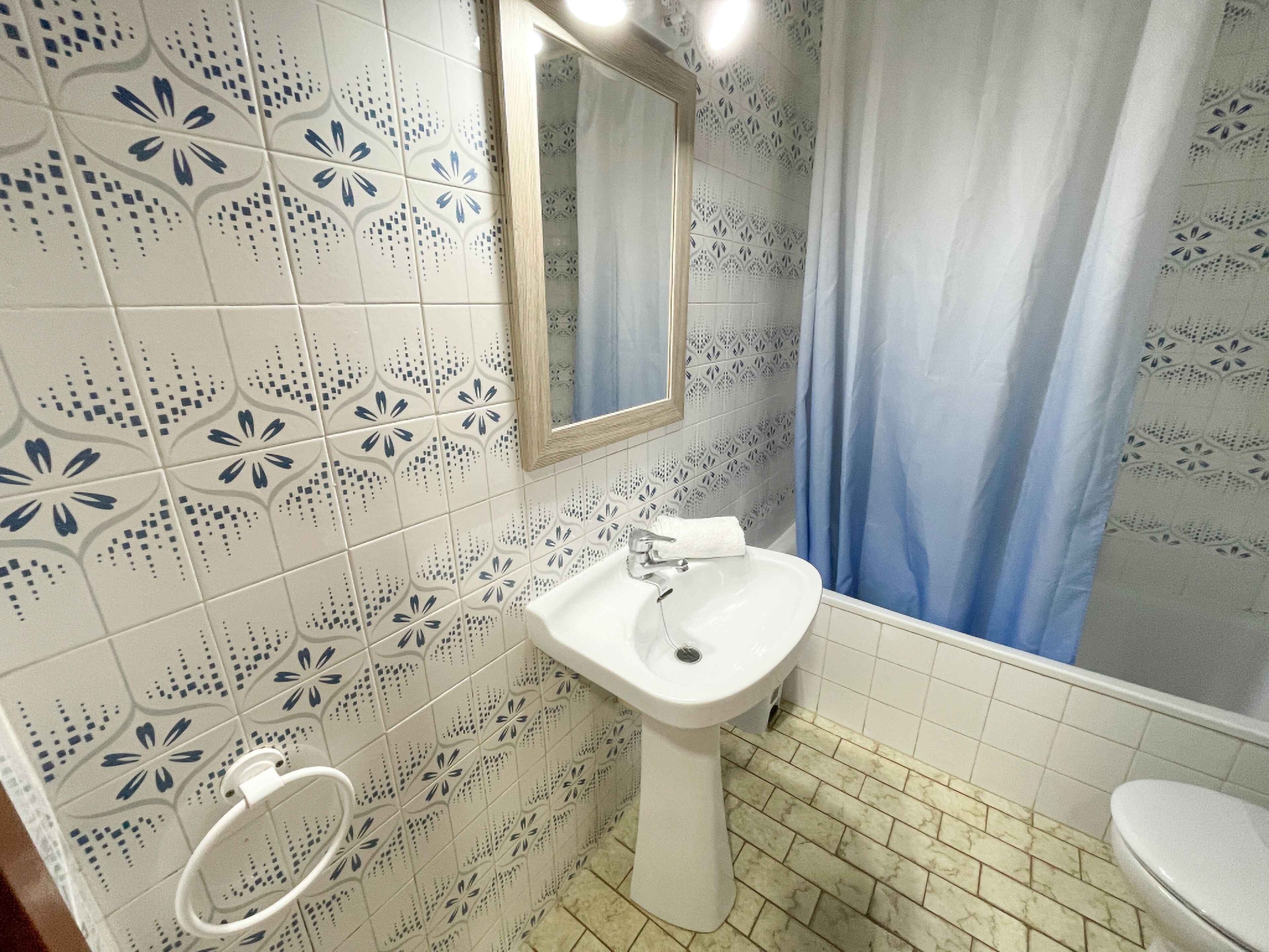 A bathroom with patterned tiles, a sink, a mirror, and a toilet.