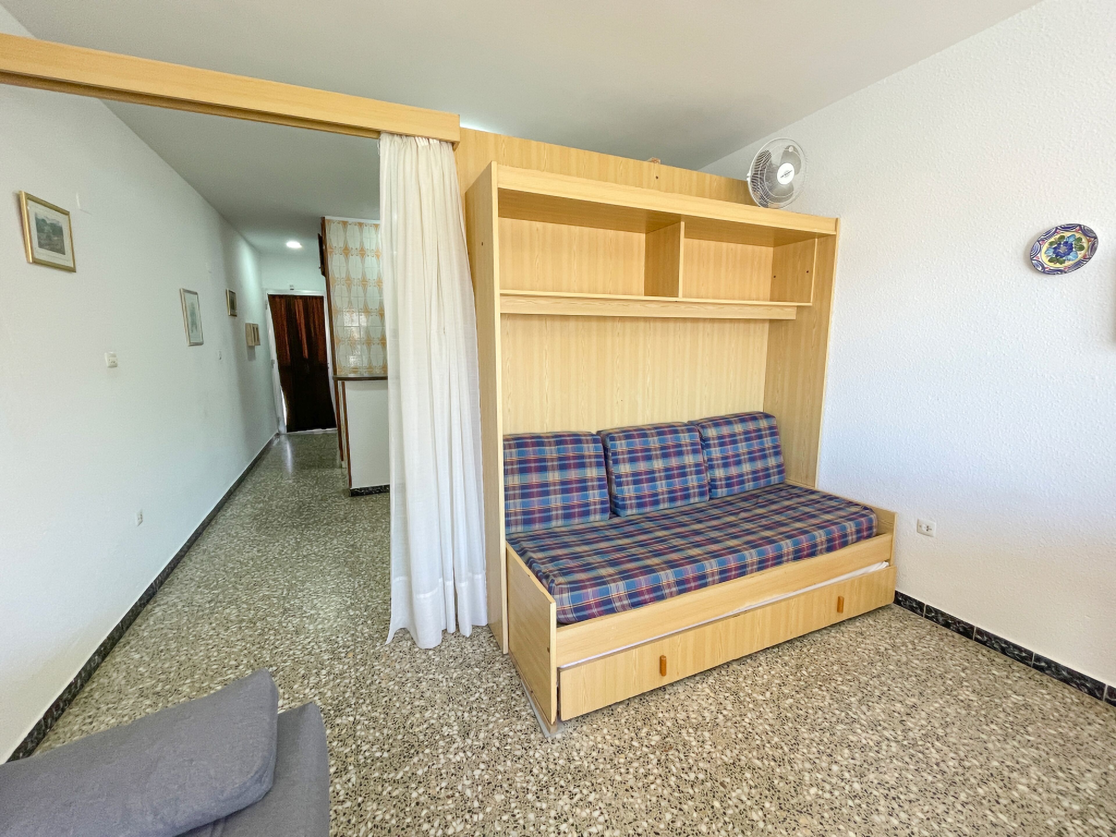 A compact room with a wooden bed, a small sofa with plaid cushions, and a ceiling fan.