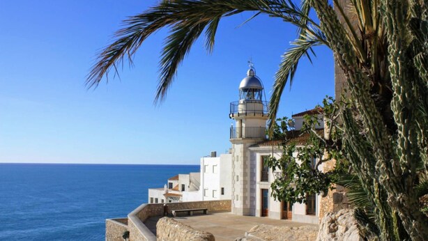 A coastal building with a lighthouse, stone walls, and a view of the sea. - Apartamentos Voramar 3000 (Peniscola)