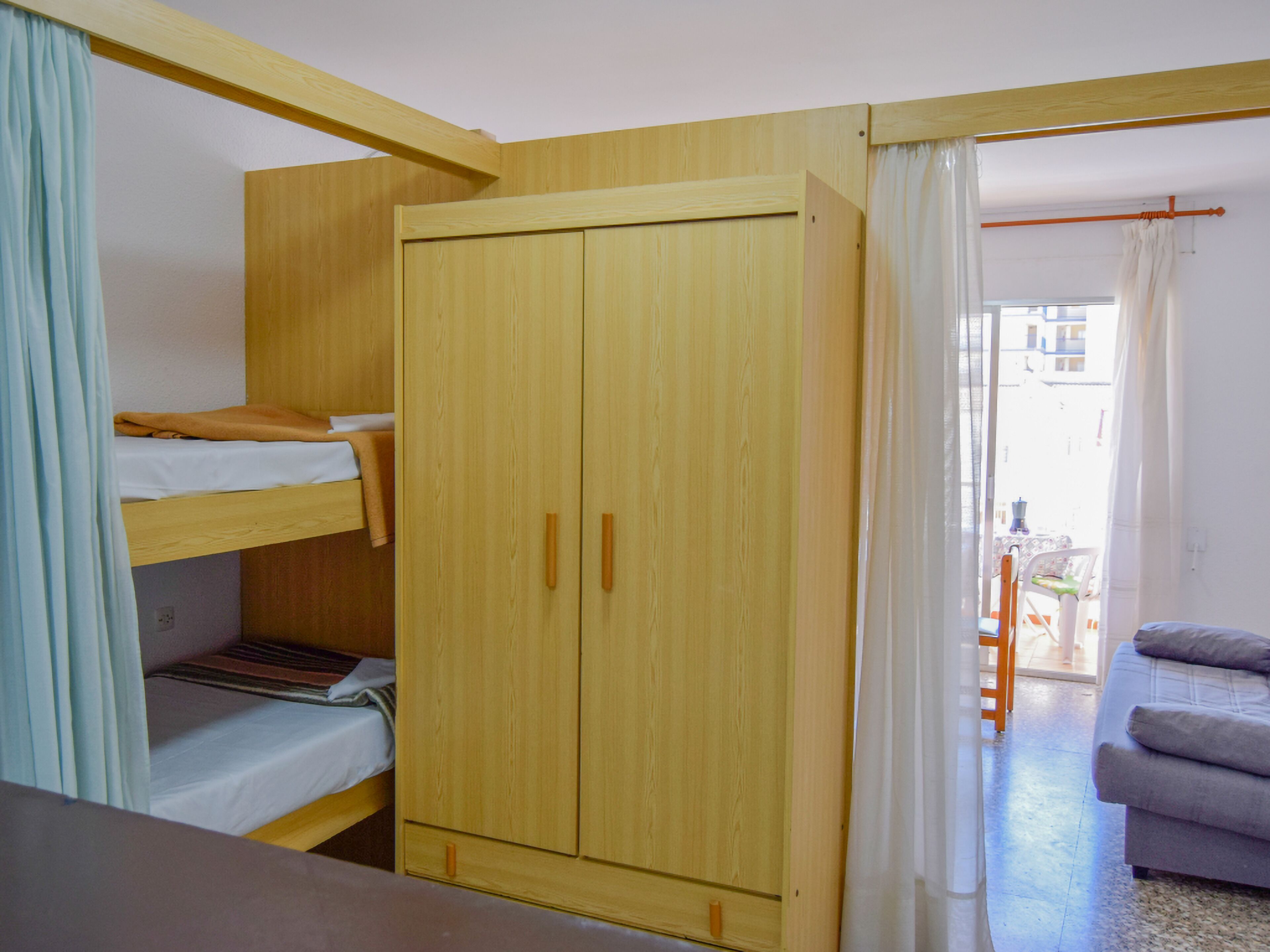 A room with bunk beds, a wooden wardrobe, a sofa, and a view of the outside.