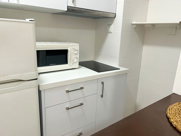 A compact kitchen with white cabinets, a microwave, and a built-in stove. - Apartamentos Voramar 3000 (Peniscola)