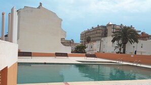 A swimming pool with two benches, a tiled deck, and a building in the background. - Apartamentos Voramar 3000 (Peniscola)