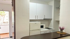 A kitchen with white cabinets, a microwave, and a small table with a decorative item. - Apartamentos Voramar 3000 (Peniscola)