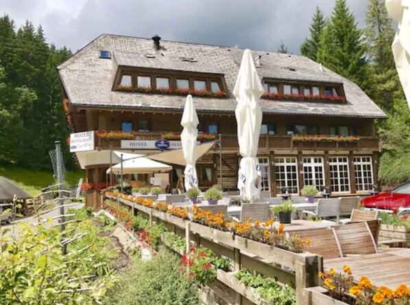 A wooden building with a balcony, a sign for a restaurant, and outdoor seating with umbrellas. - Kräuter Chalet (Furtwangen)