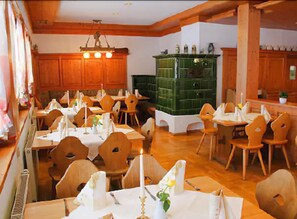 A dining area with wooden tables and chairs, a green cabinet, and a chandelier. - Kräuter Chalet (Furtwangen)